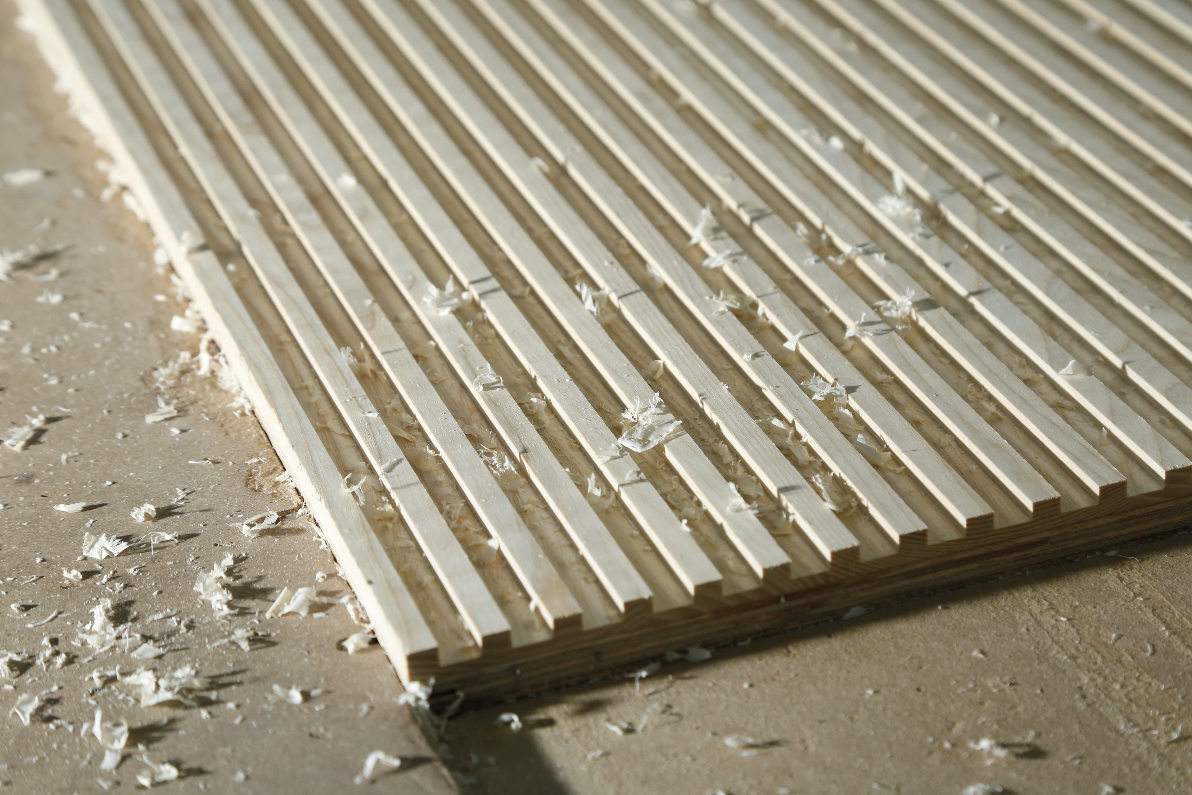 Close up of Ash wood fluted wall panel with wood shavings, as if to imply freshly fluted. By Element